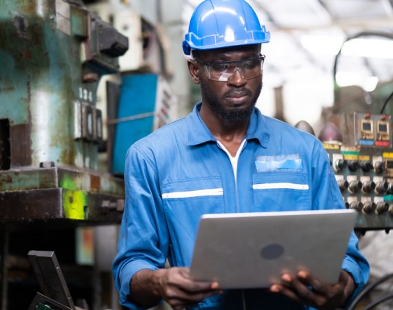Male Engineer Working on laptop computer in Factory. black male engineer checking Quality control the condition of the machine. Service and maintenance of factory machinery